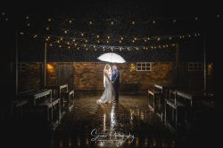 donington park farmhouse wedding photography bride groom outside in courtyard raining with umbrella creative photo